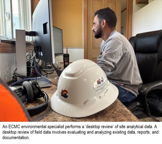 ECMC employee viewing a computer, ECMC branded hard hat in the foreground