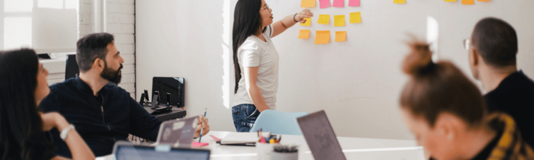 People in a meeting as a woman presents on a whiteboard.